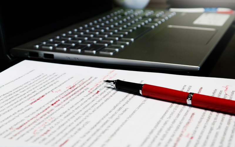 Lektorat und Korrektorat: Der Feinschliff, der den Unterschied macht | Ein roter Kugelschreiber liegt auf dem rot lektoriertem Manusscript