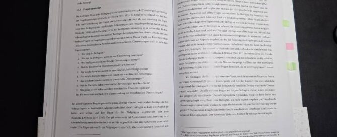 Eine aufgeschlagene Masterarbeit liegt auf einem schwarzen Tisch.